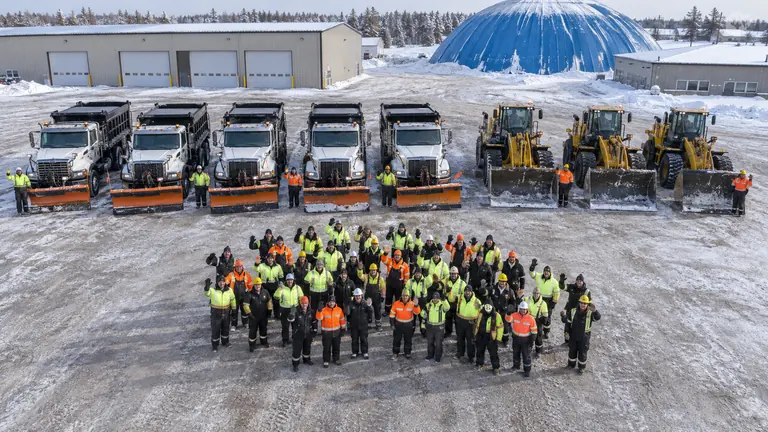 Snow and ice crew posing in front of plow trucks and loaders at a winter supply yard