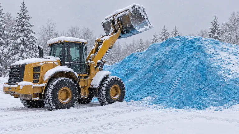 Wheel loader beside a large pile of blue treated road salt in heavy snow